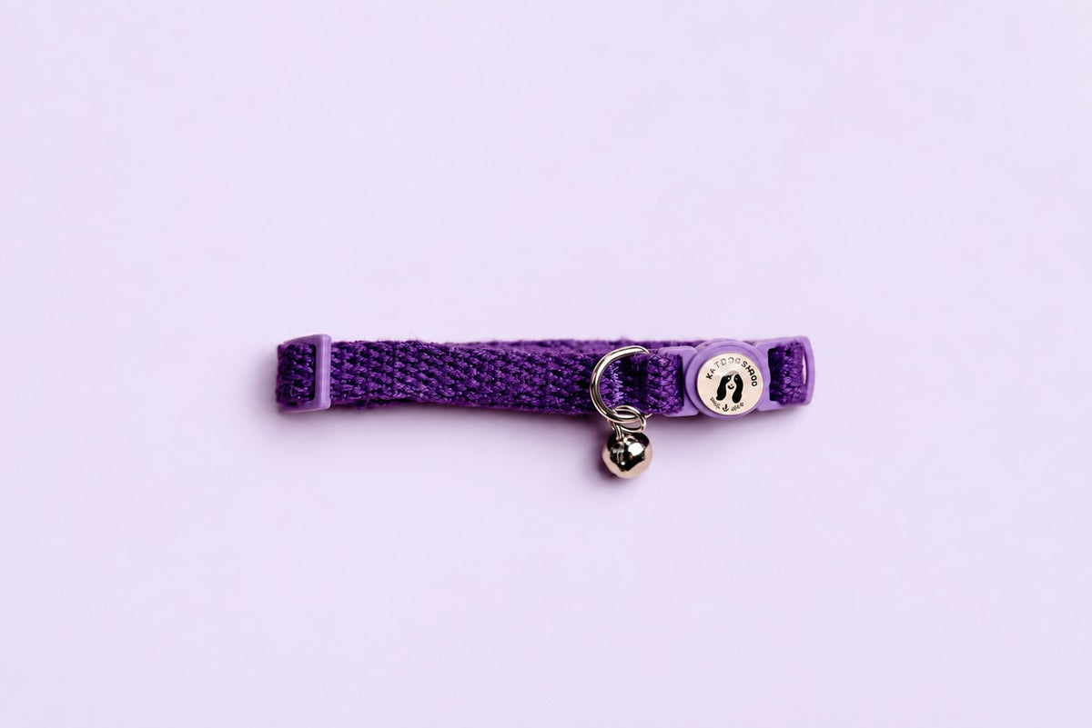 Salt Dog Studios indigo purple hemp cat collar with matching breakaway buckle, logo and silver bell on a pale lavender background.